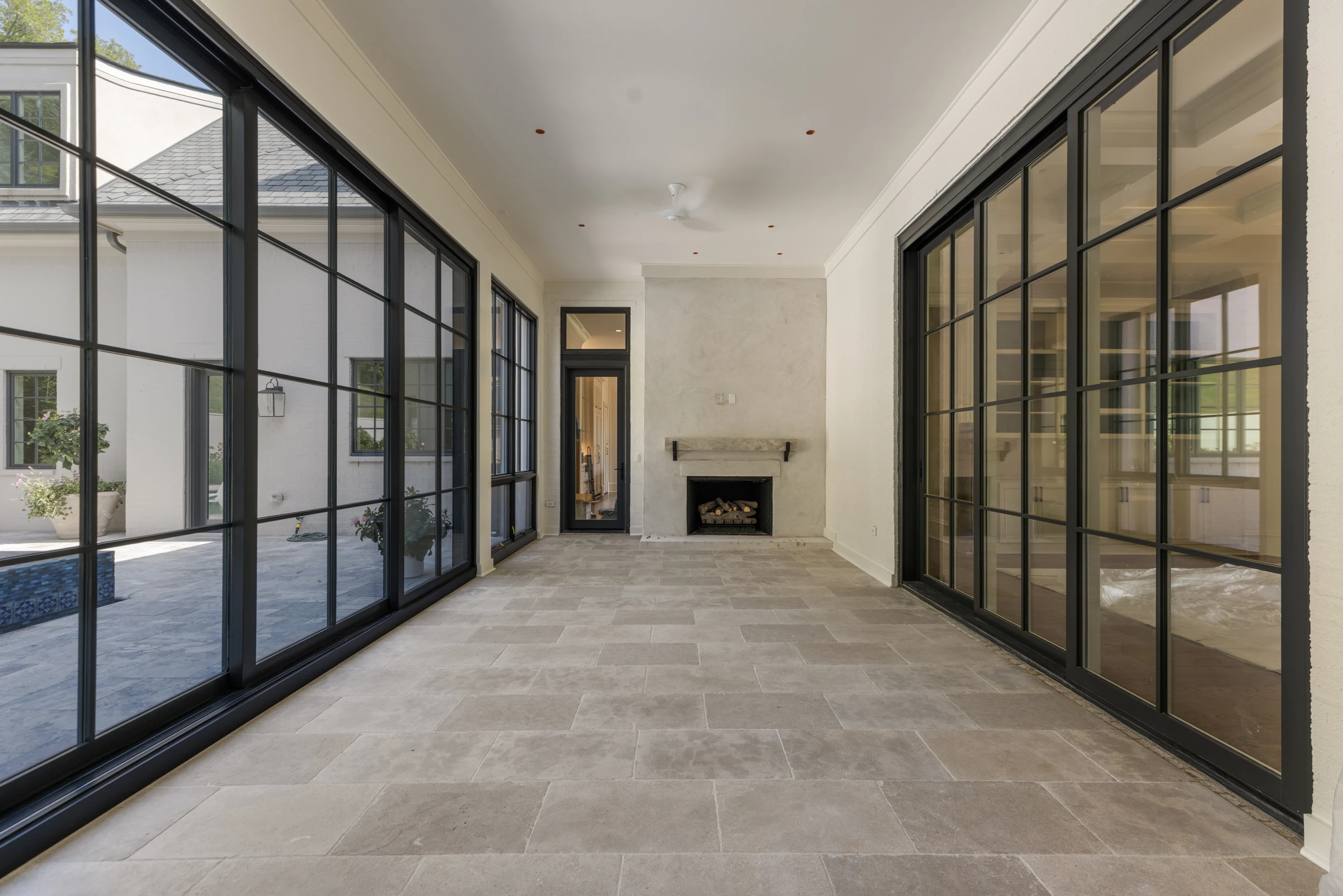 Sunroom with limestone flooring, black-framed glass doors, and a stone fireplace